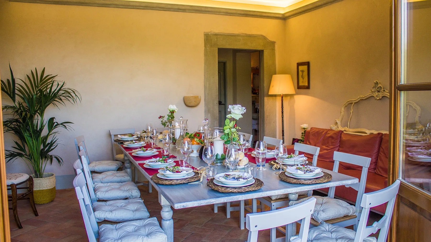 A dining room with a long table set with dishes and surrounded by seating.