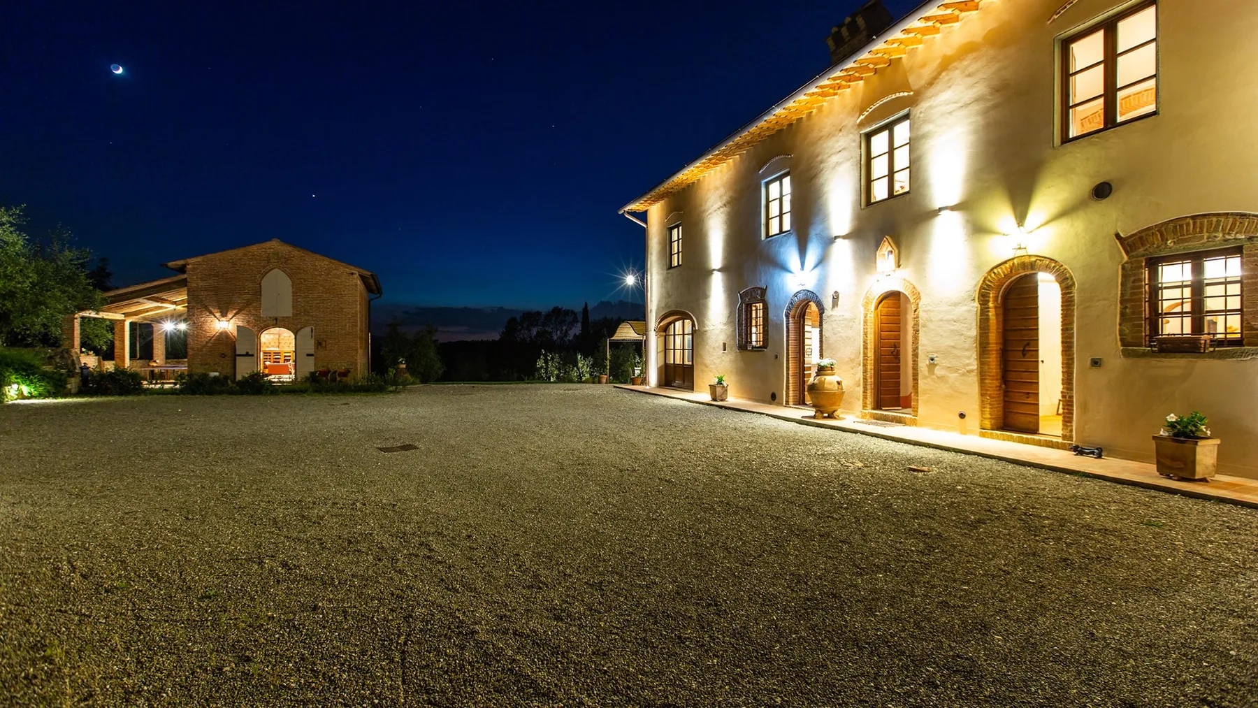 A warmly lit building faces a broad gravel courtyard at night.