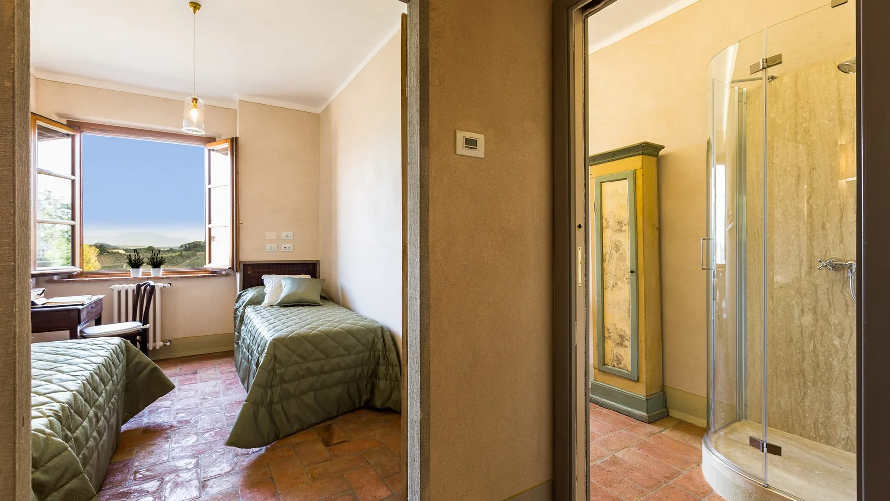 A bedroom with two beds sits beside a bathroom with a glass shower.