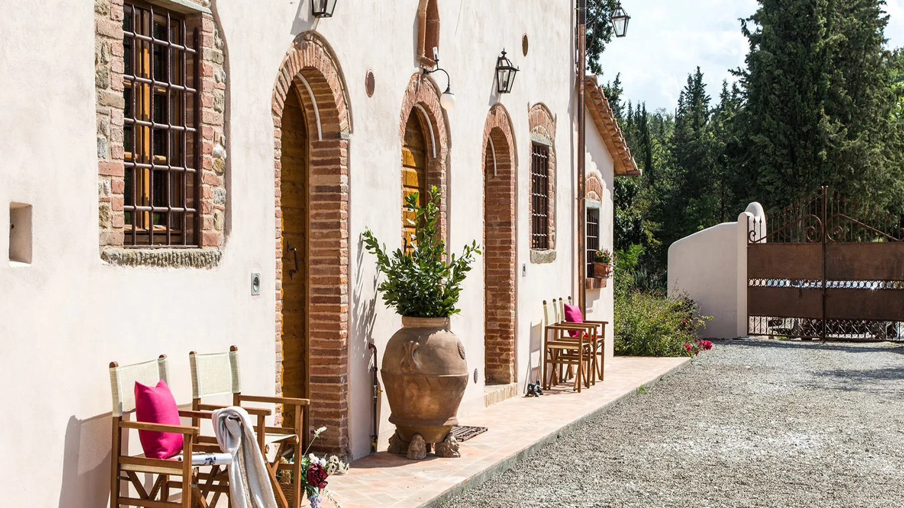 A courtyard beside a pale stucco building, with arched doorways and outdoor seating.