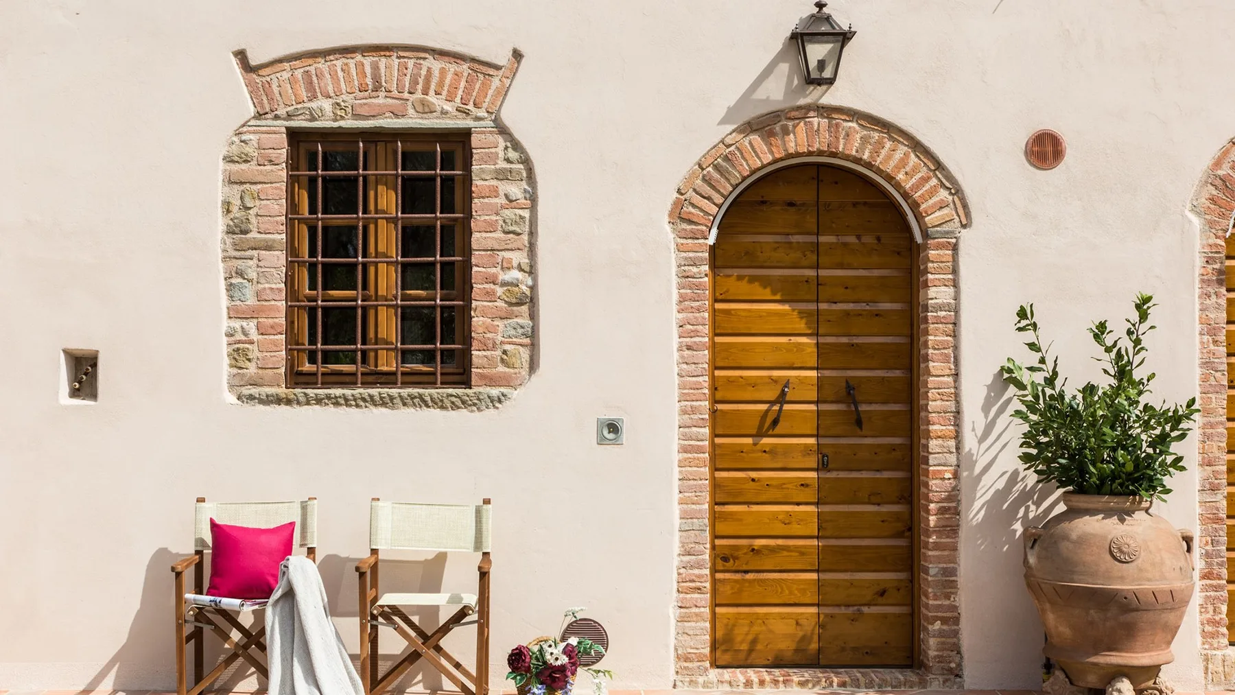 A white stucco facade with an arched wooden door and a barred window.
