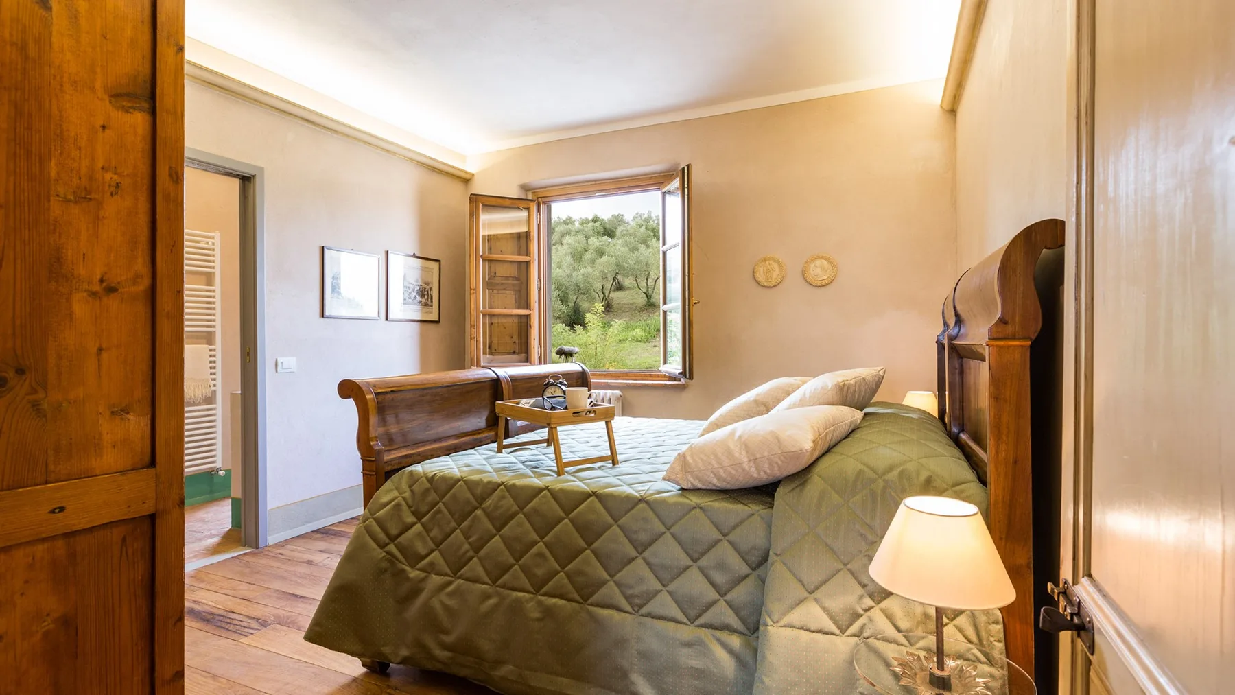 A bedroom with a quilted bedspread and an open window overlooking greenery.