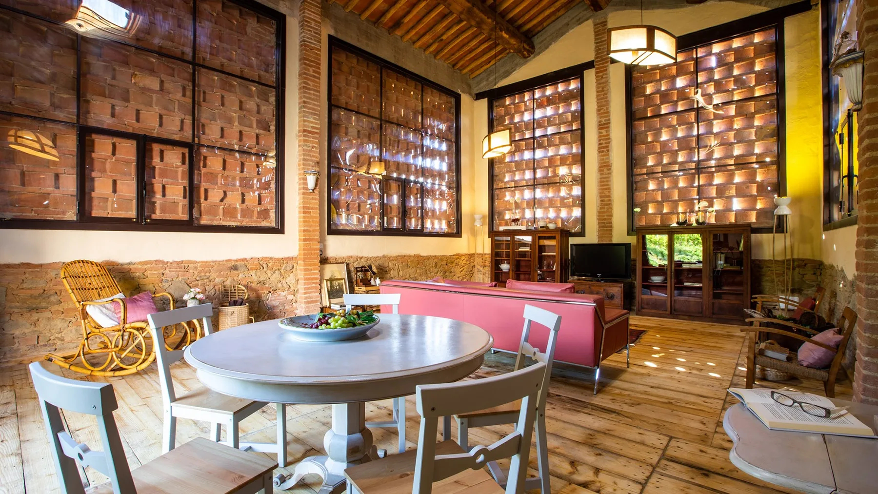 A rustic living room with a round table and red seating beneath a timber ceiling.