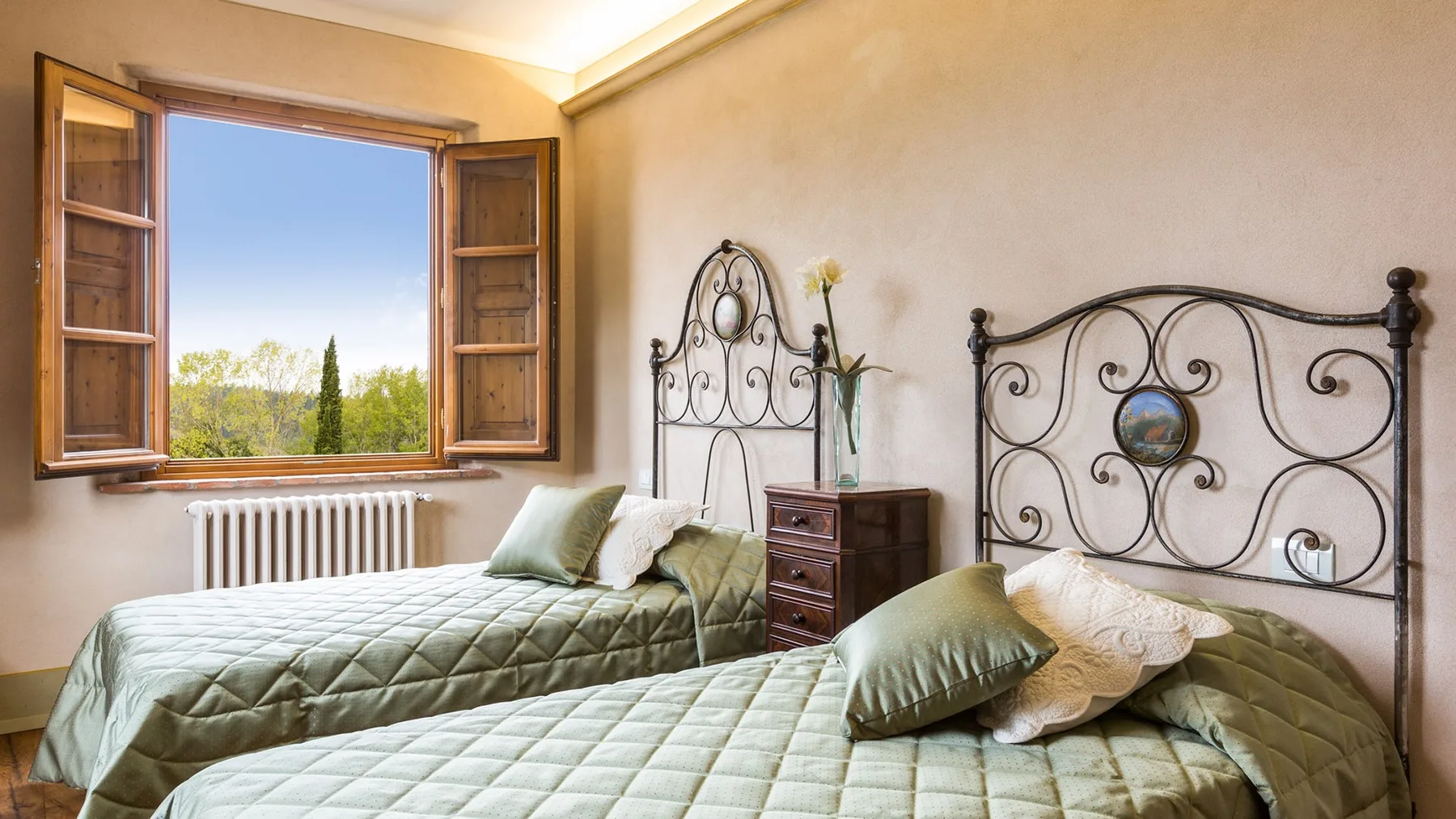 A bedroom with two beds beside an open window overlooking greenery.