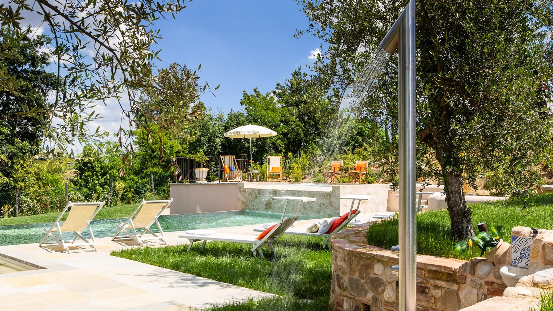 An outdoor swimming pool sits among lounge chairs, greenery, and patio seating.