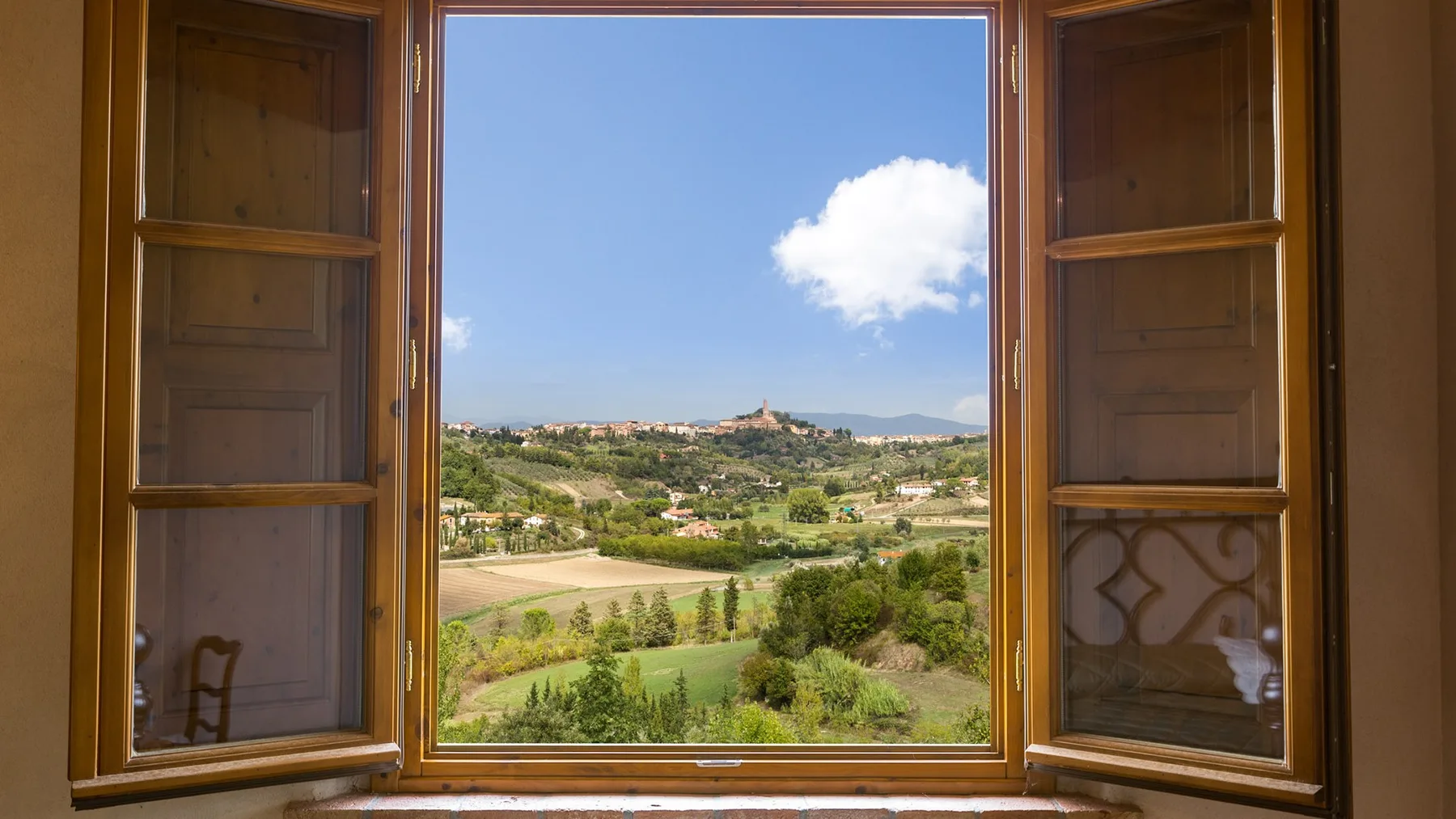 An open window frames a countryside landscape with fields and a blue sky.