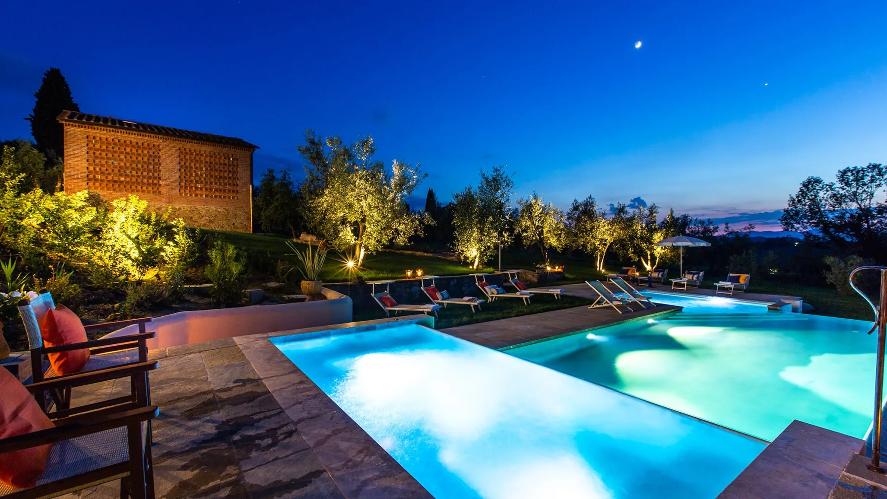 An outdoor swimming pool glows beneath the evening sky, with lounge seating nearby.