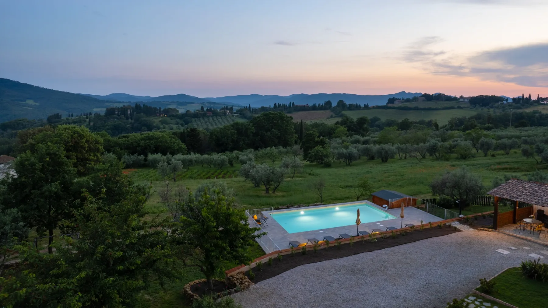 An outdoor swimming pool overlooks green countryside at dusk.