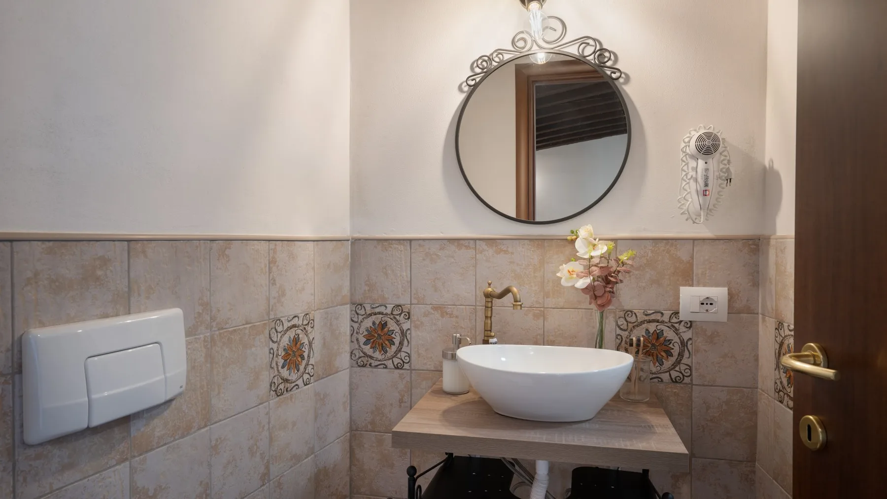 A bathroom vanity with a white vessel sink, round mirror, and tiled walls.