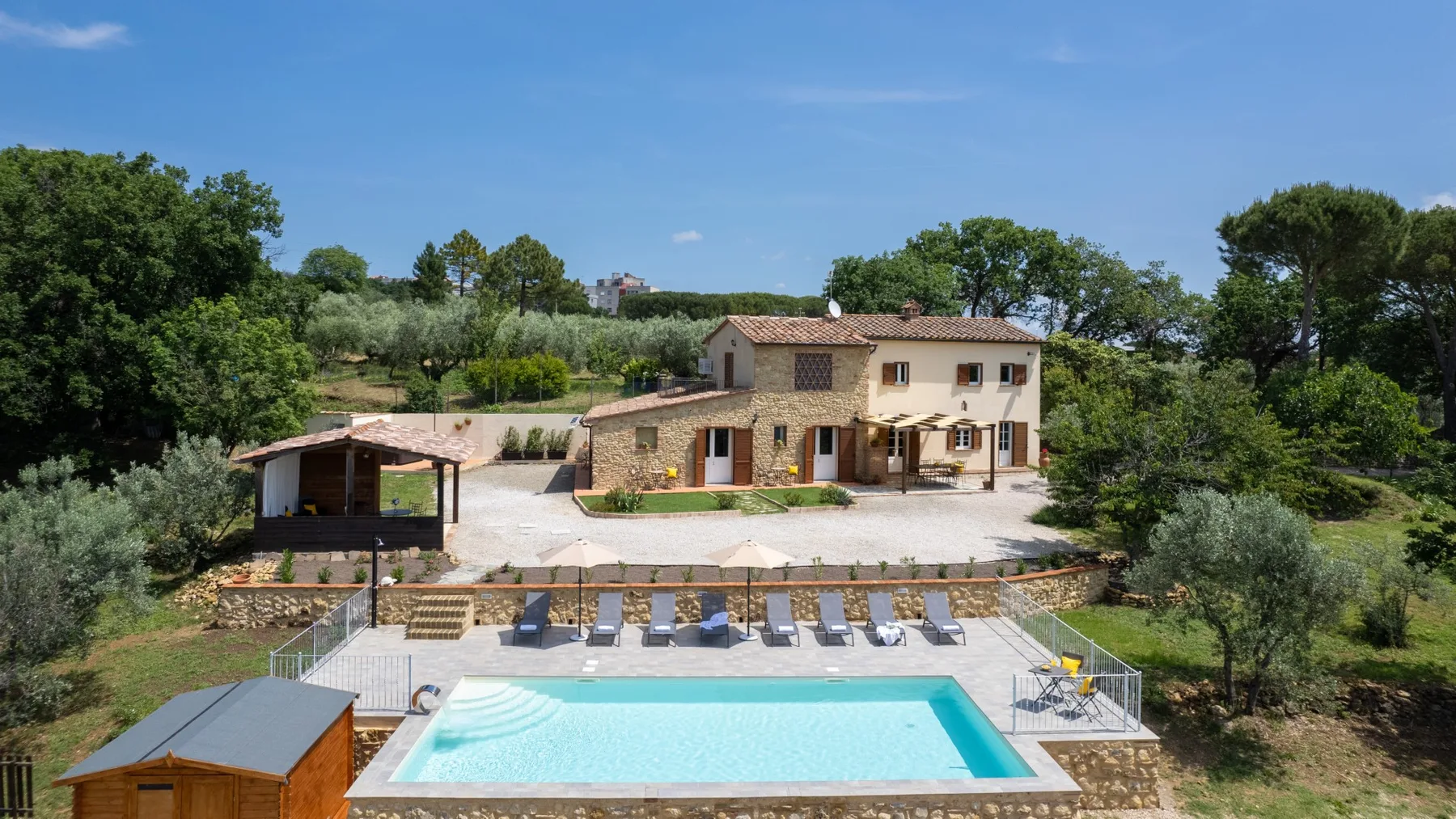 A countryside house overlooks a swimming pool and surrounding greenery.