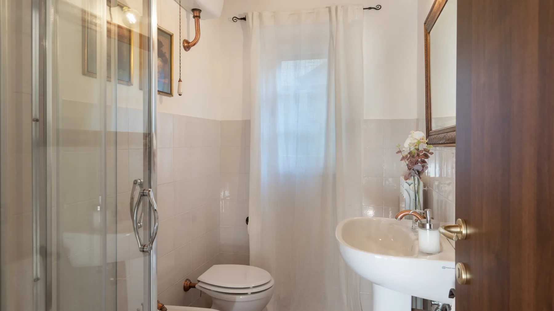 A bathroom with a shower, toilet, and sink beneath a curtained window.