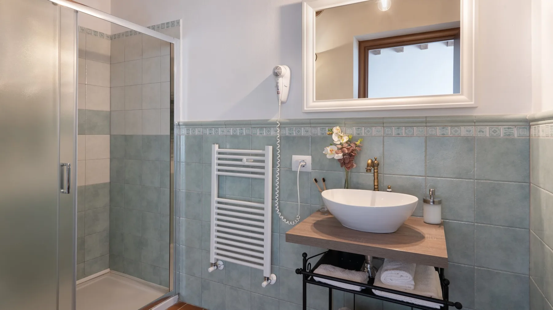 A bathroom with a glass shower, wall-mounted towel warmer, and vessel sink.