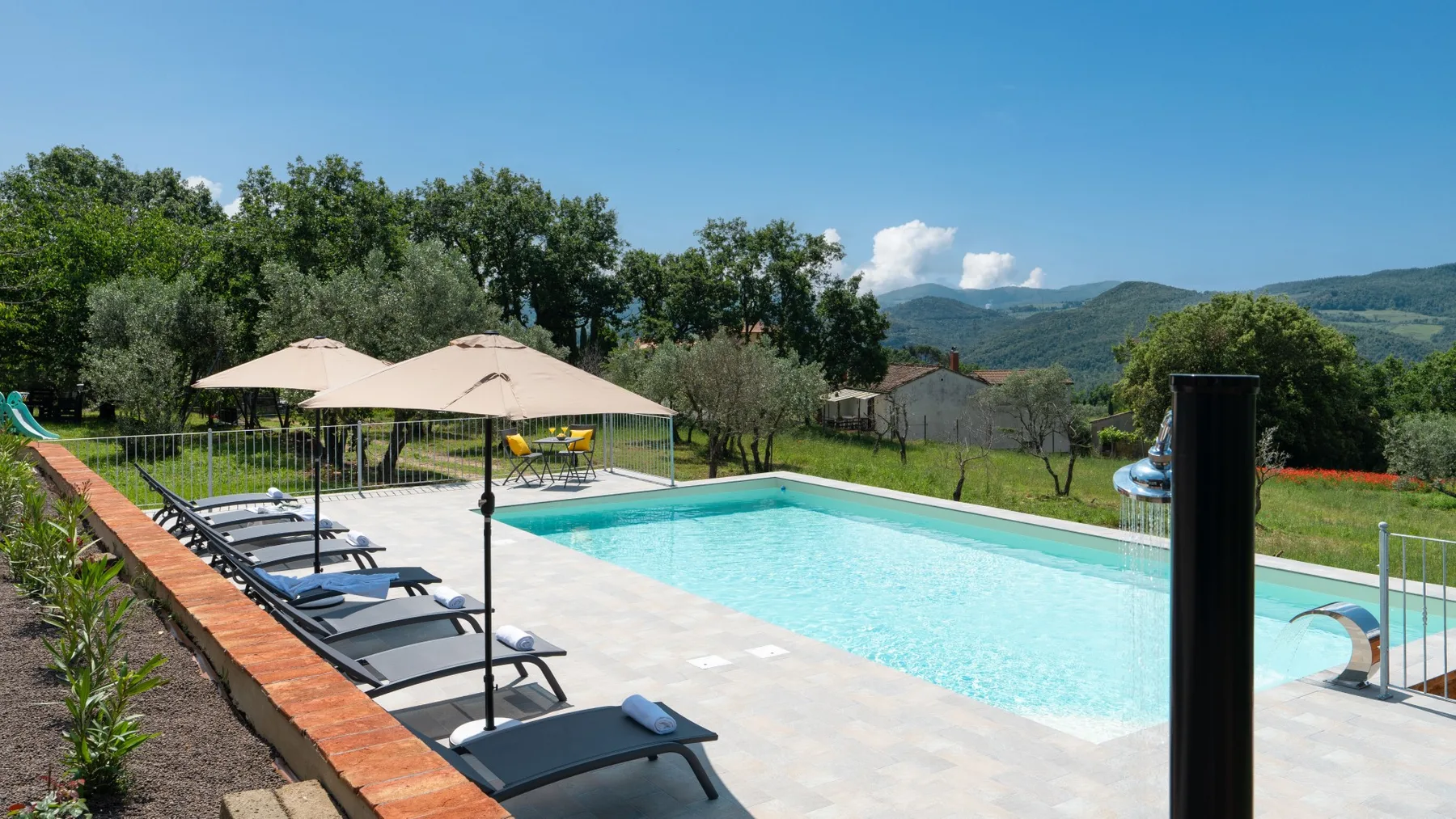 An outdoor swimming pool sits beside a paved deck with loungers and umbrellas.