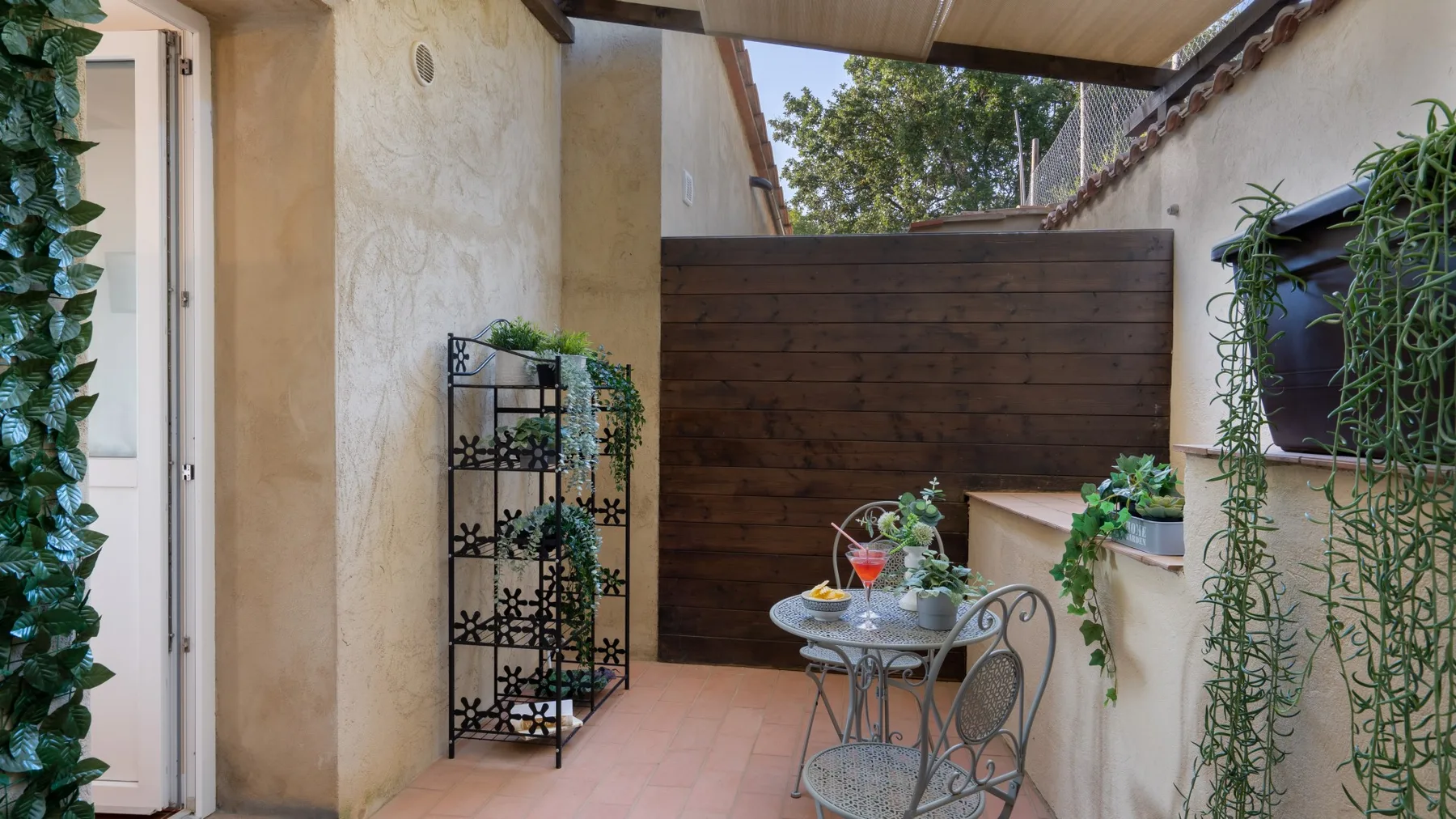 A small outdoor patio has a table and chairs beside a wooden privacy screen.