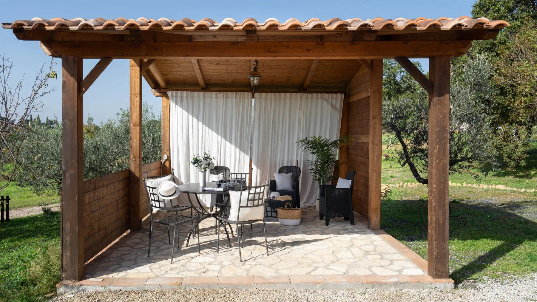 A covered outdoor seating area with a table and chairs beneath a wooden canopy.