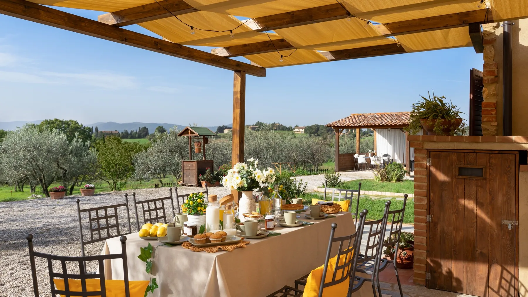An outdoor dining area under a wooden pergola, with a table set for a meal.
