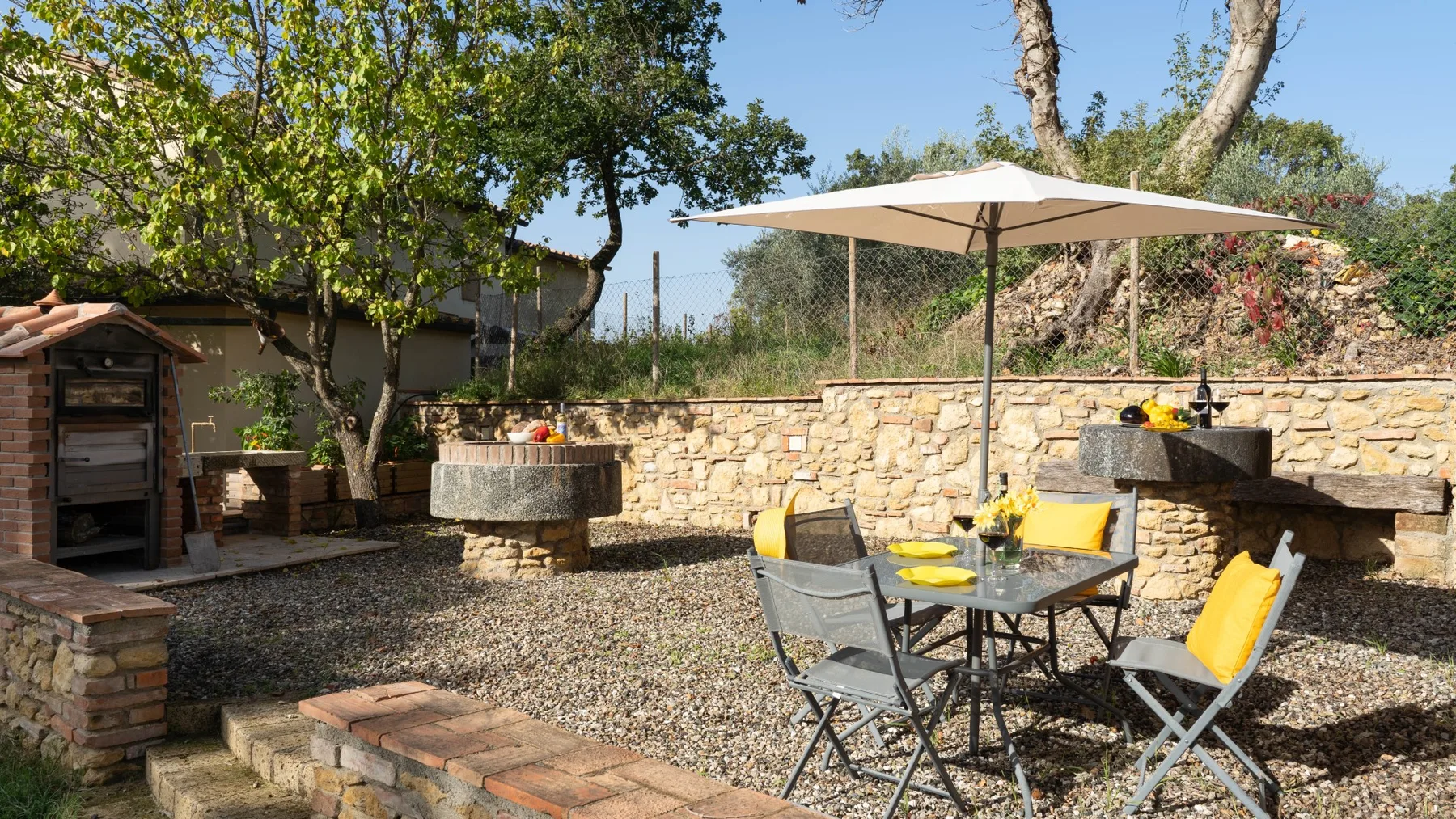 A gravel outdoor dining area with a table, seating, and a large umbrella.