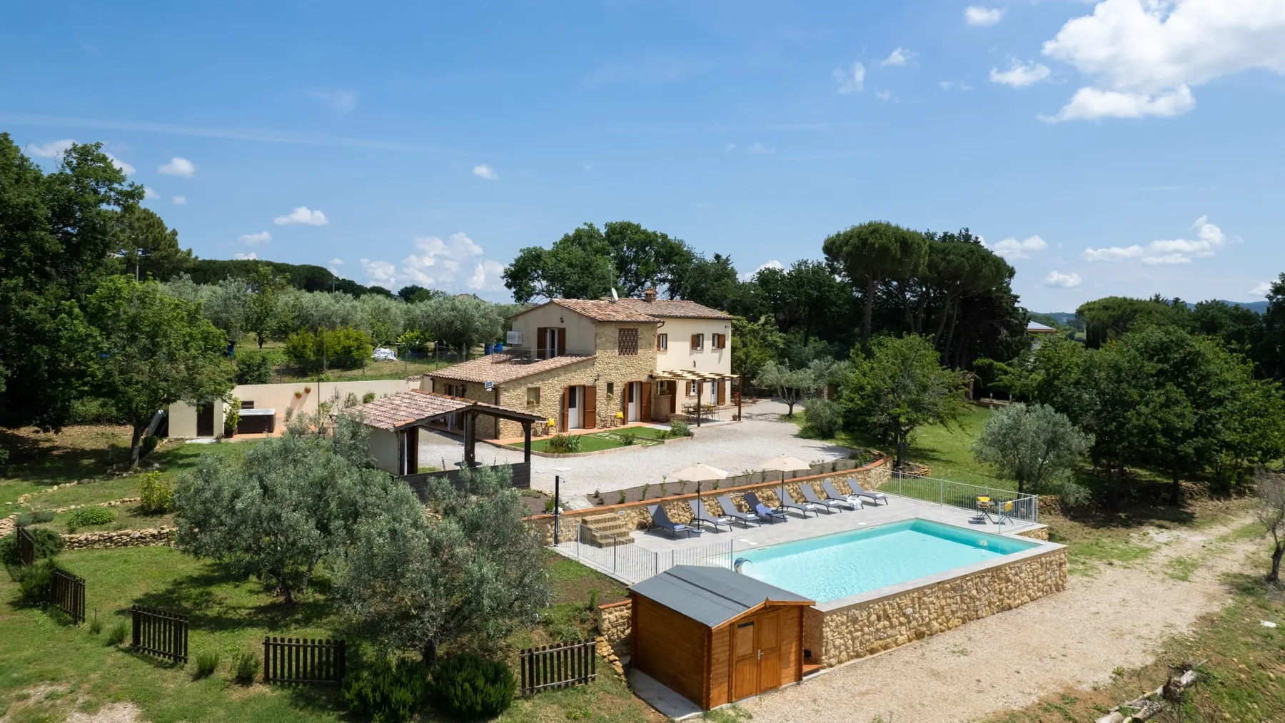 A swimming pool and surrounding grounds sit beside a house amid green trees.