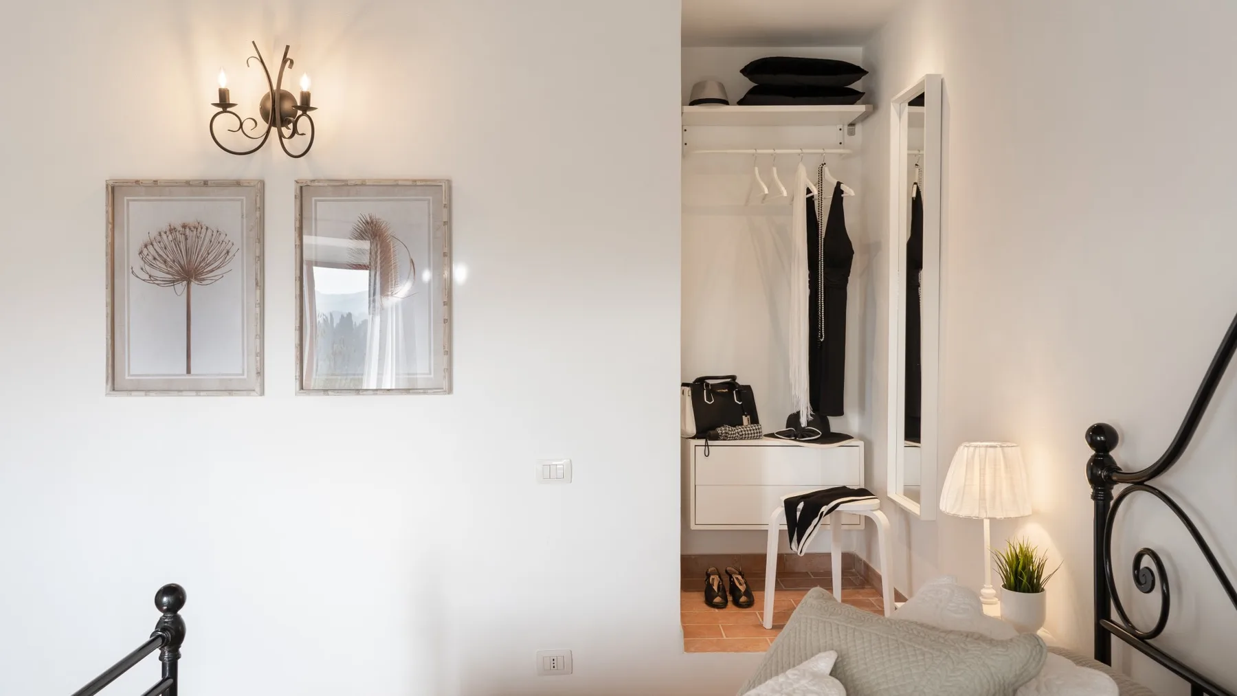A bright bedroom with a bed beside an open wardrobe and framed wall art.