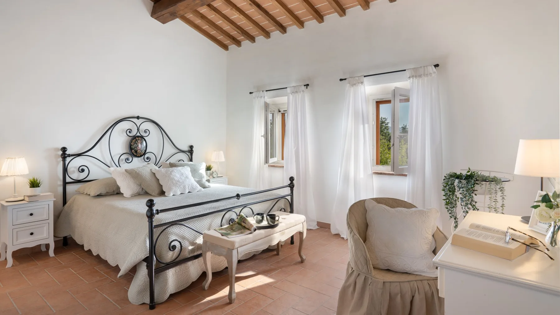 A bright bedroom with a metal-framed bed and two windows with sheer curtains.