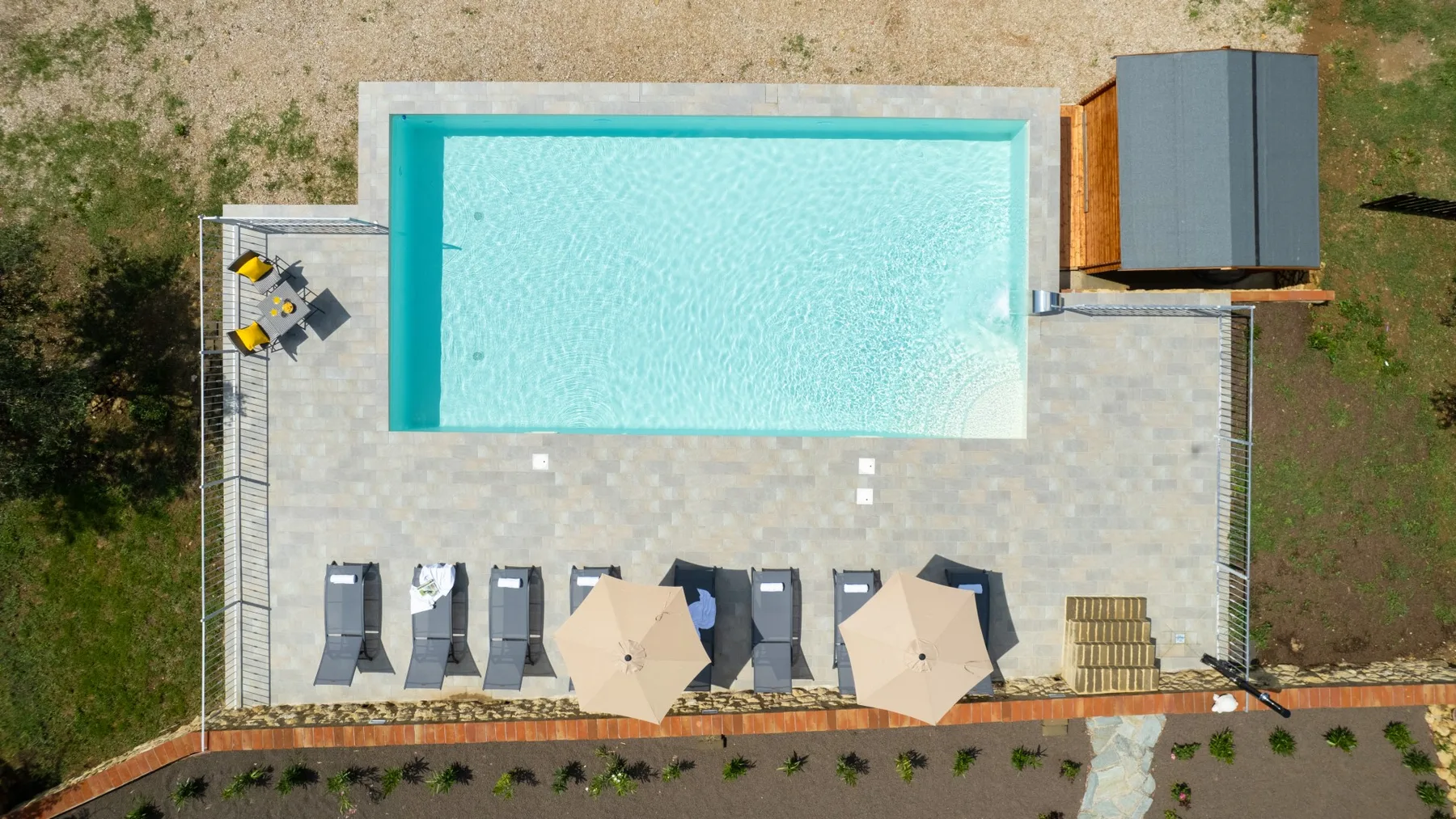 An outdoor swimming pool sits beside a paved patio with lounge chairs and umbrellas.