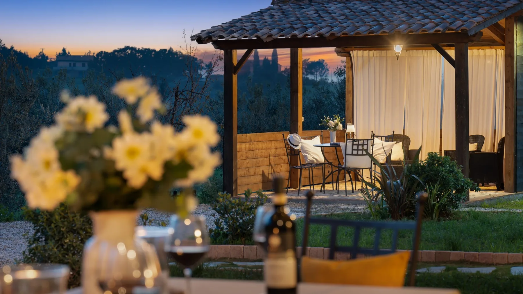 A covered outdoor seating area overlooks a garden at dusk.