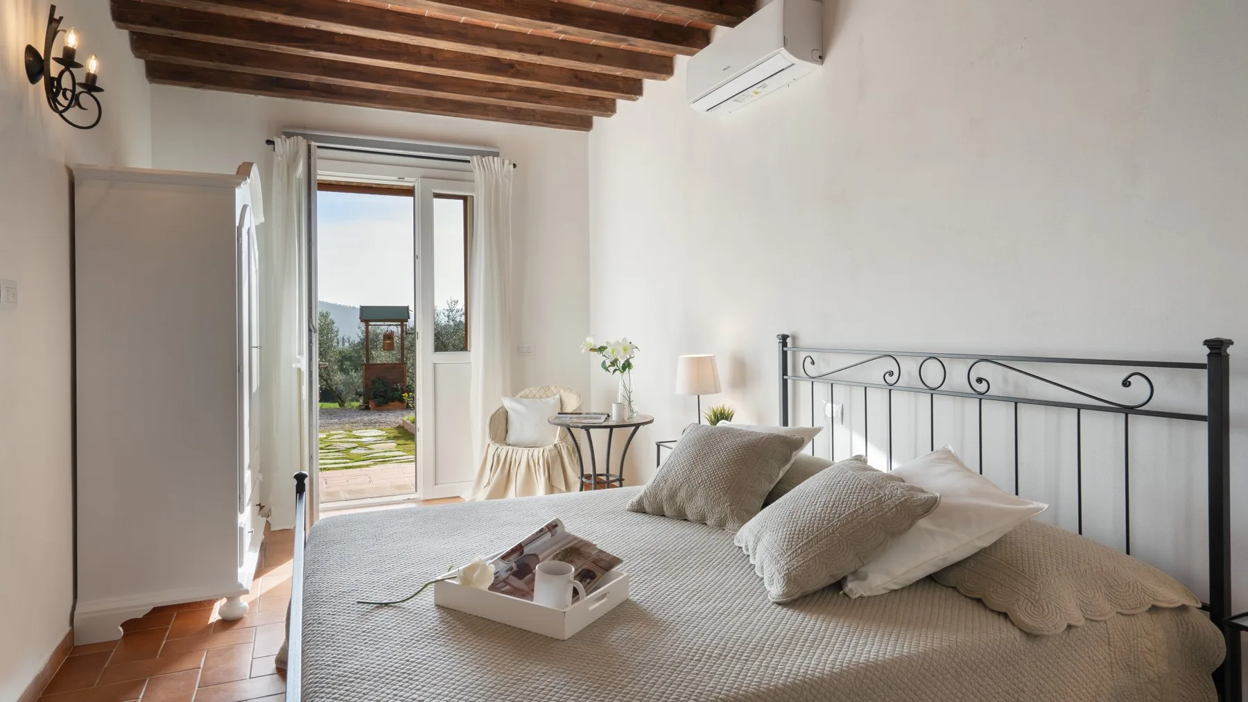 A bedroom with a bed, a black metal headboard, and open doors to a patio.