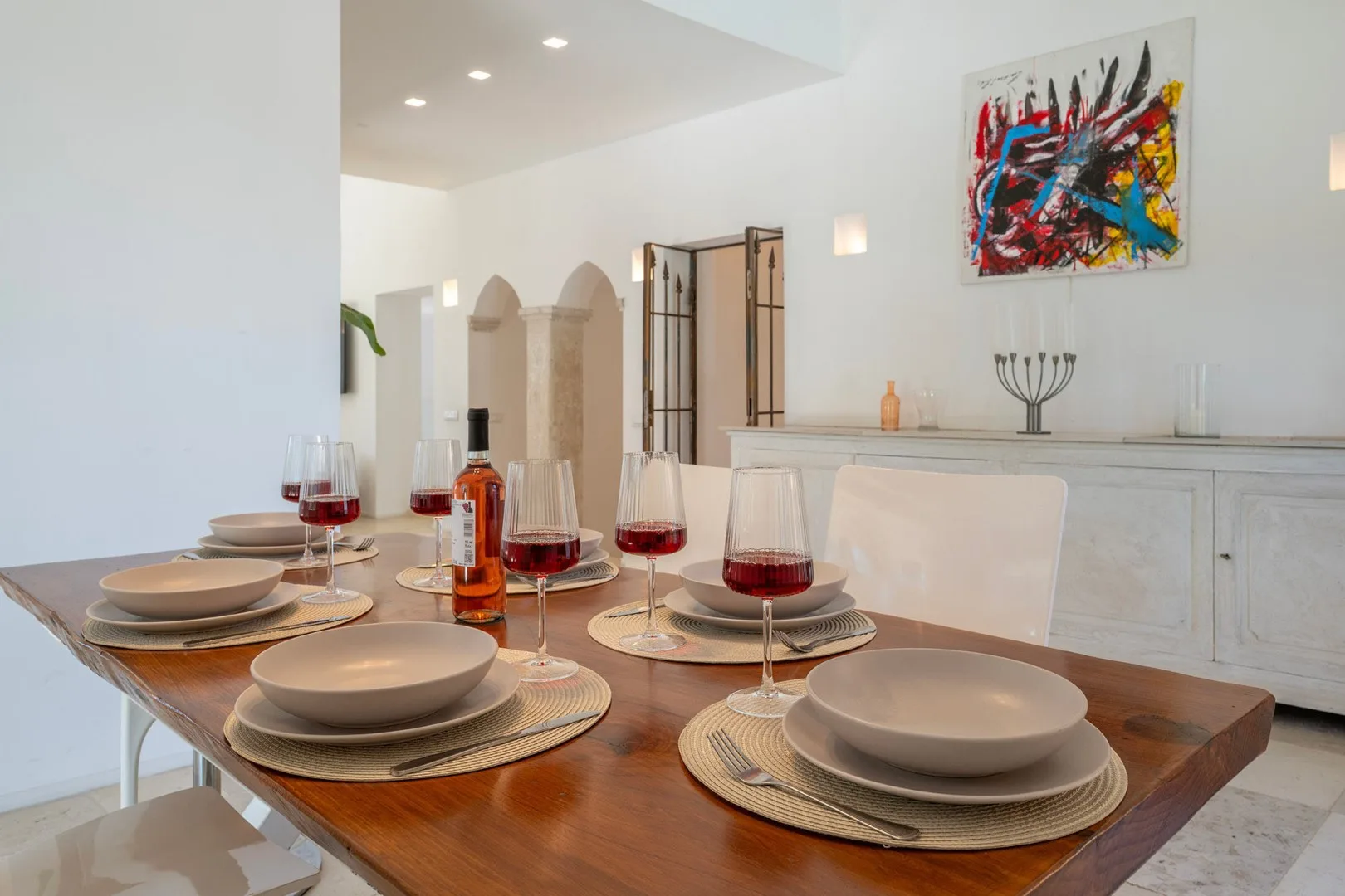 A dining table set with plates and glasses sits beneath colorful abstract artwork.