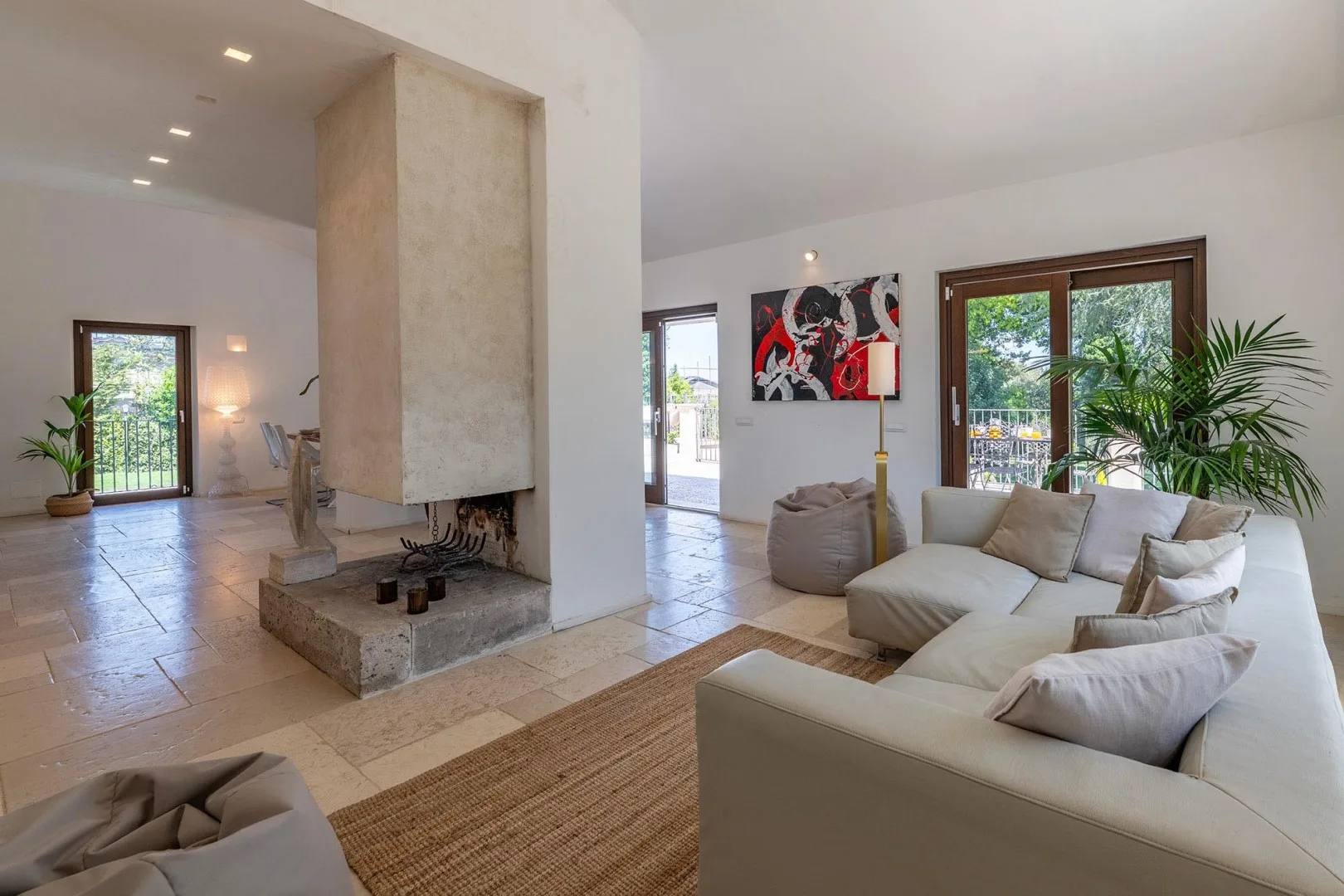 A bright living room with a white sectional sofa and a central stone fireplace.