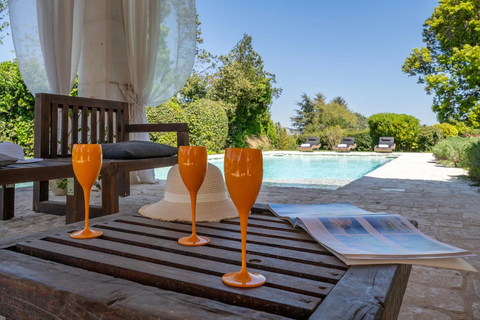 A poolside seating area overlooks a swimming pool surrounded by greenery.
