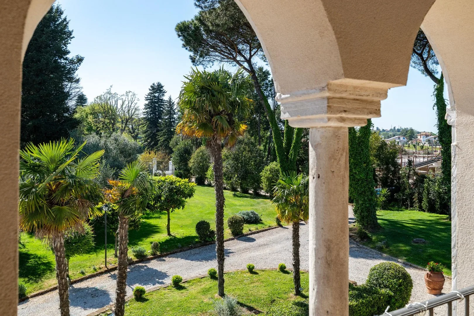 A stone-arched terrace overlooks a green garden with palm trees.