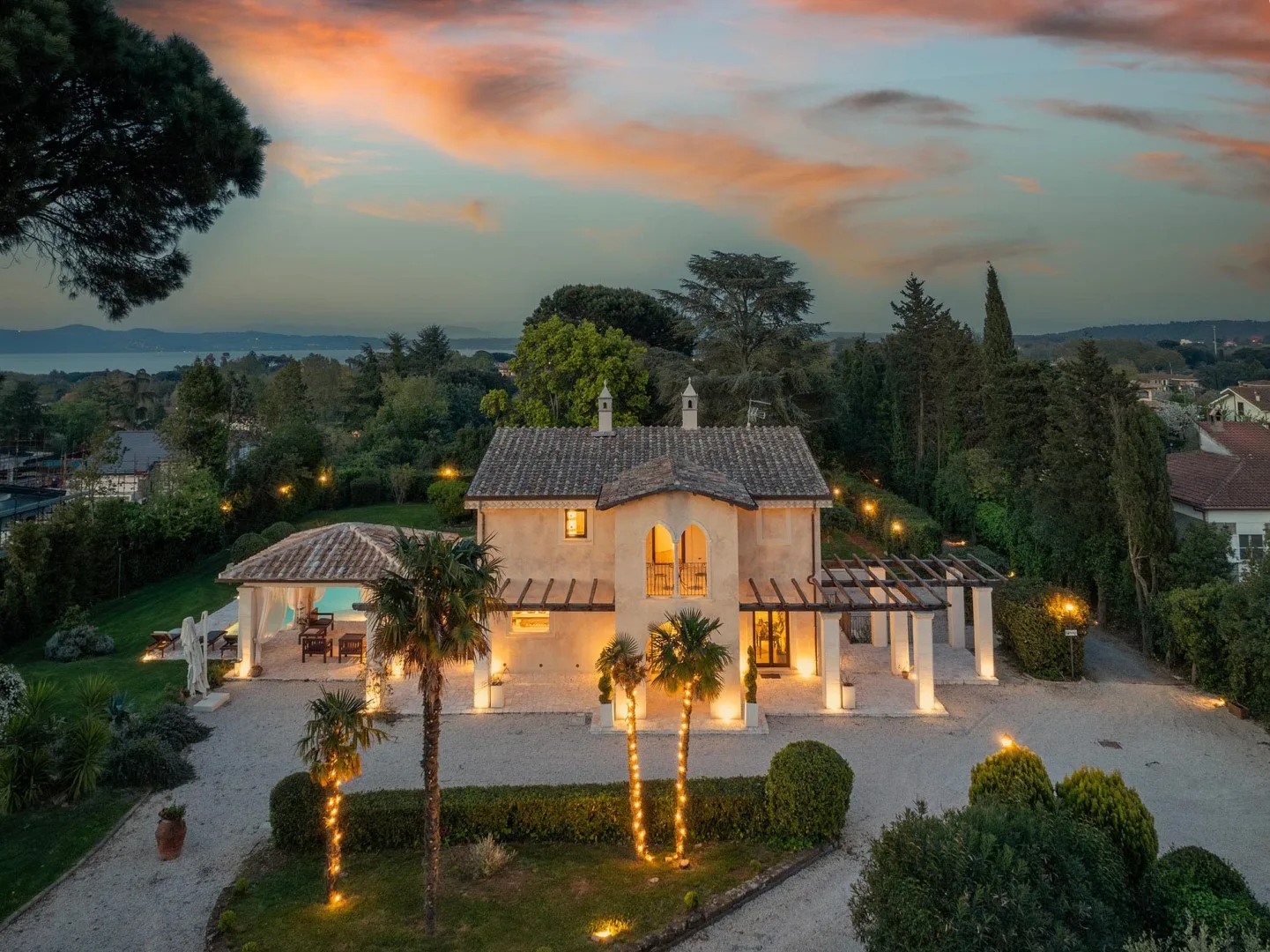 A warmly lit house stands among landscaped gardens beneath a colorful evening sky.