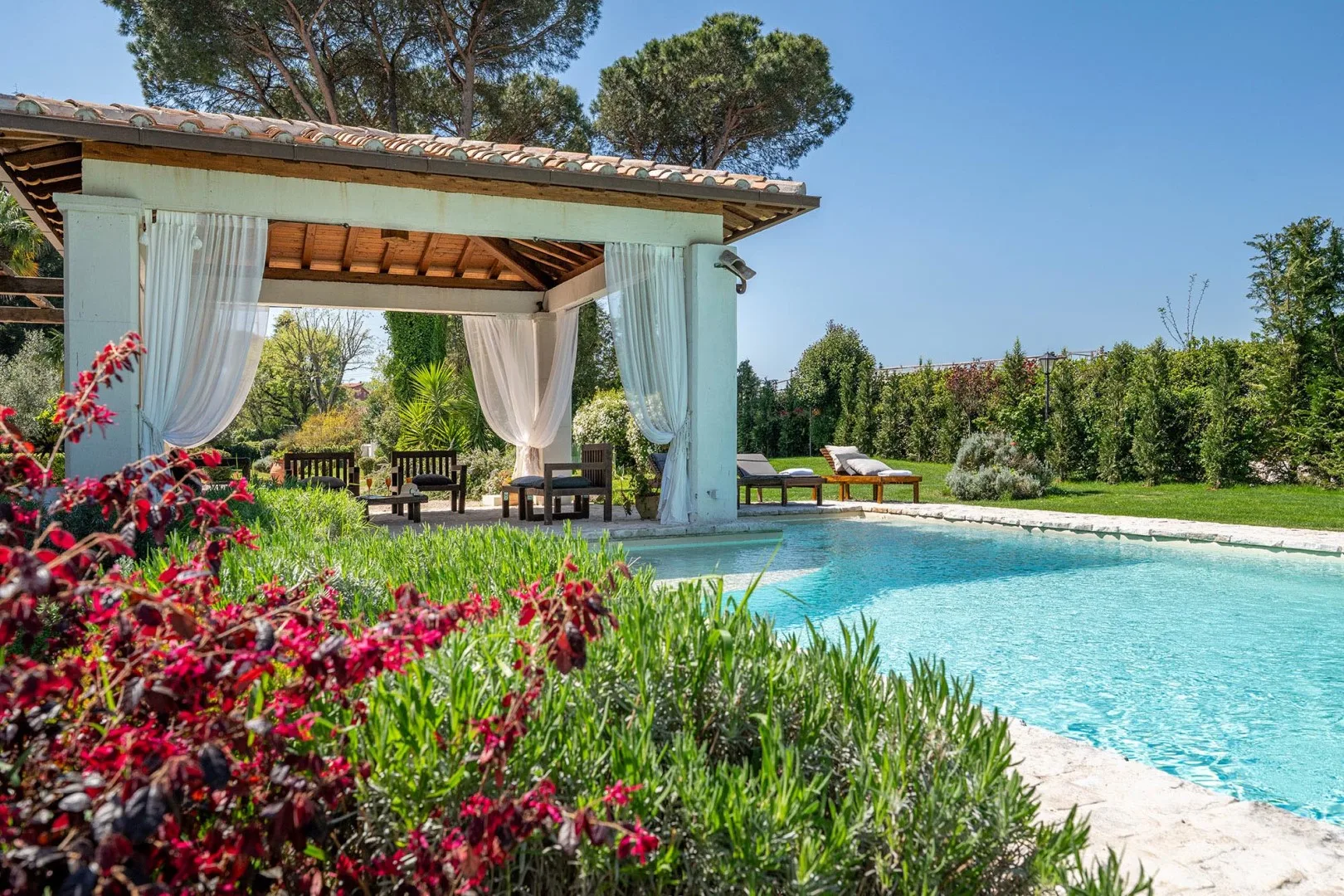 A garden pool beside a shaded pavilion with flowing curtains.