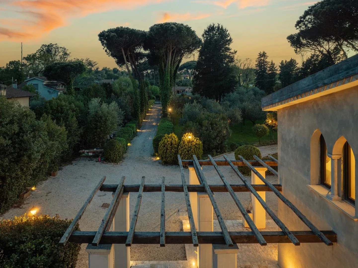 A landscaped garden and pathway at dusk, with a pergola in the foreground.