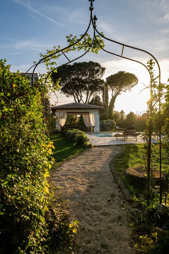 A garden path leads to a shaded seating area beside a swimming pool.