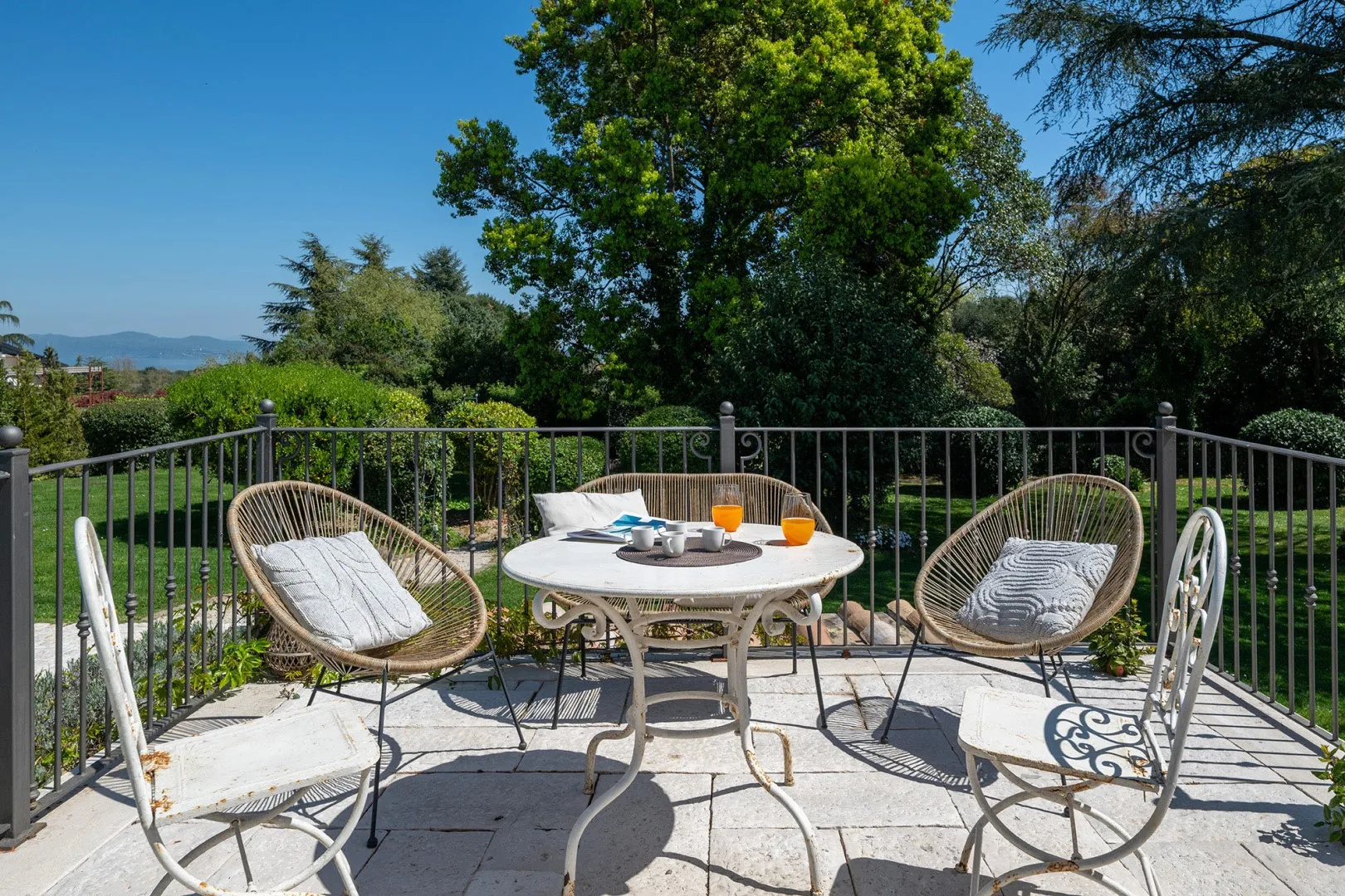 A patio seating area with a round table and chairs overlooks a leafy garden.