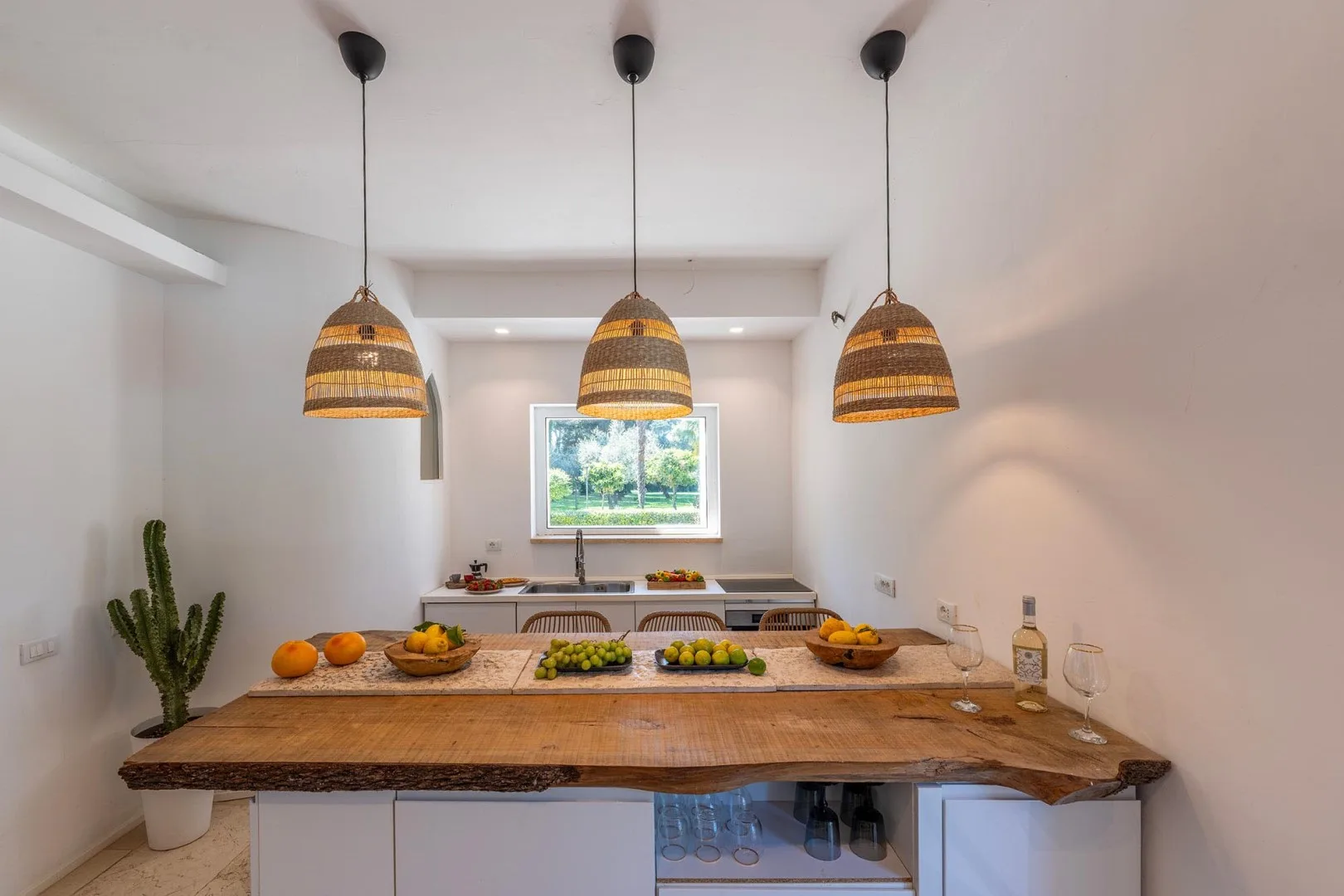 A bright kitchen with a long wooden counter beneath three pendant lights.