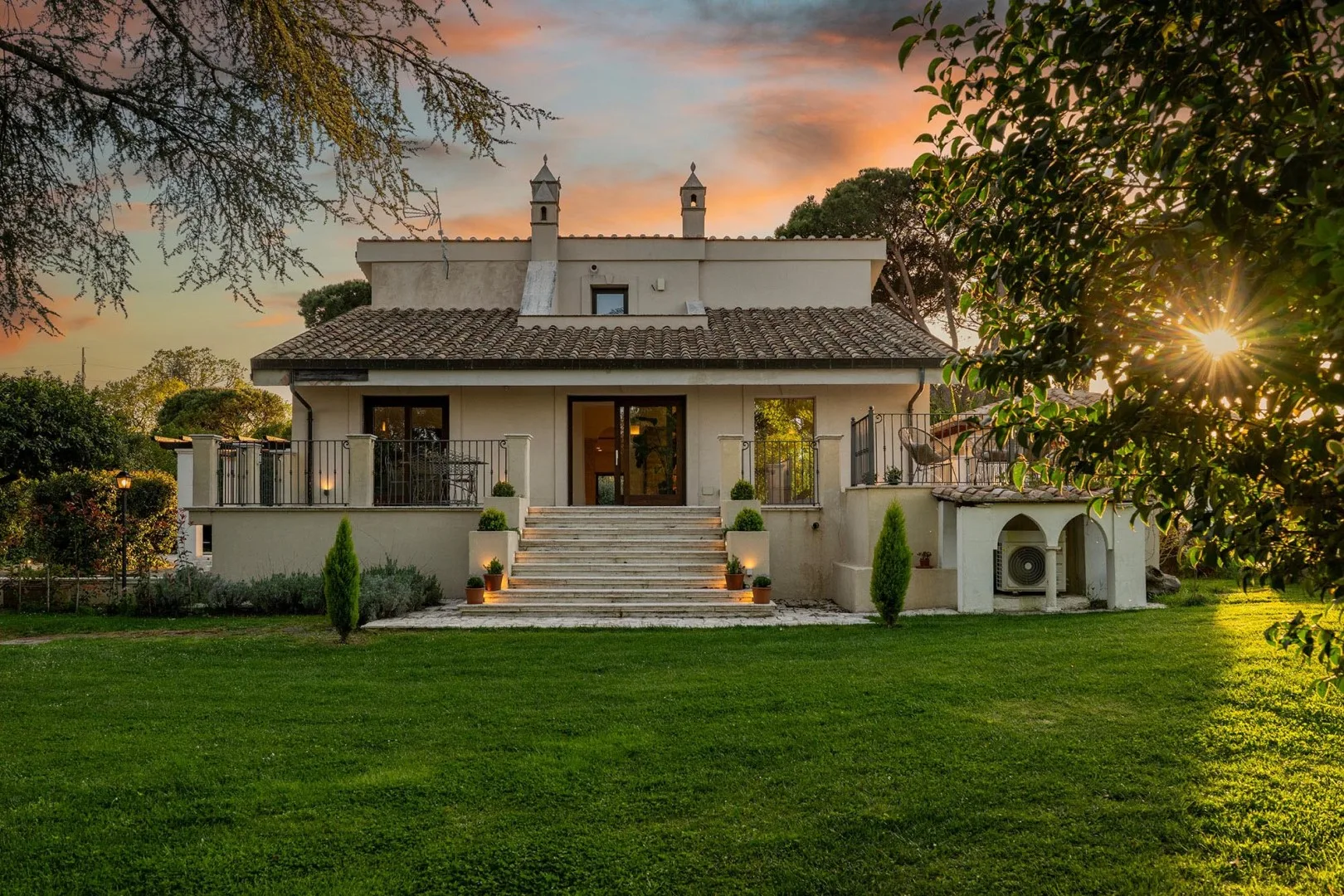 A large house with a raised terrace and lawn at sunset.