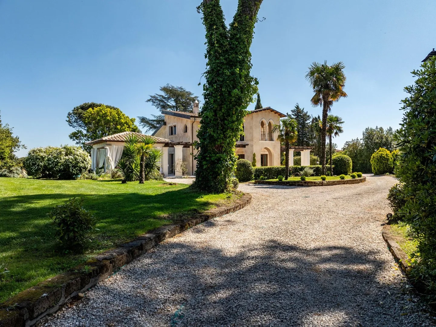 A gravel driveway curves toward a large house set among landscaped gardens.