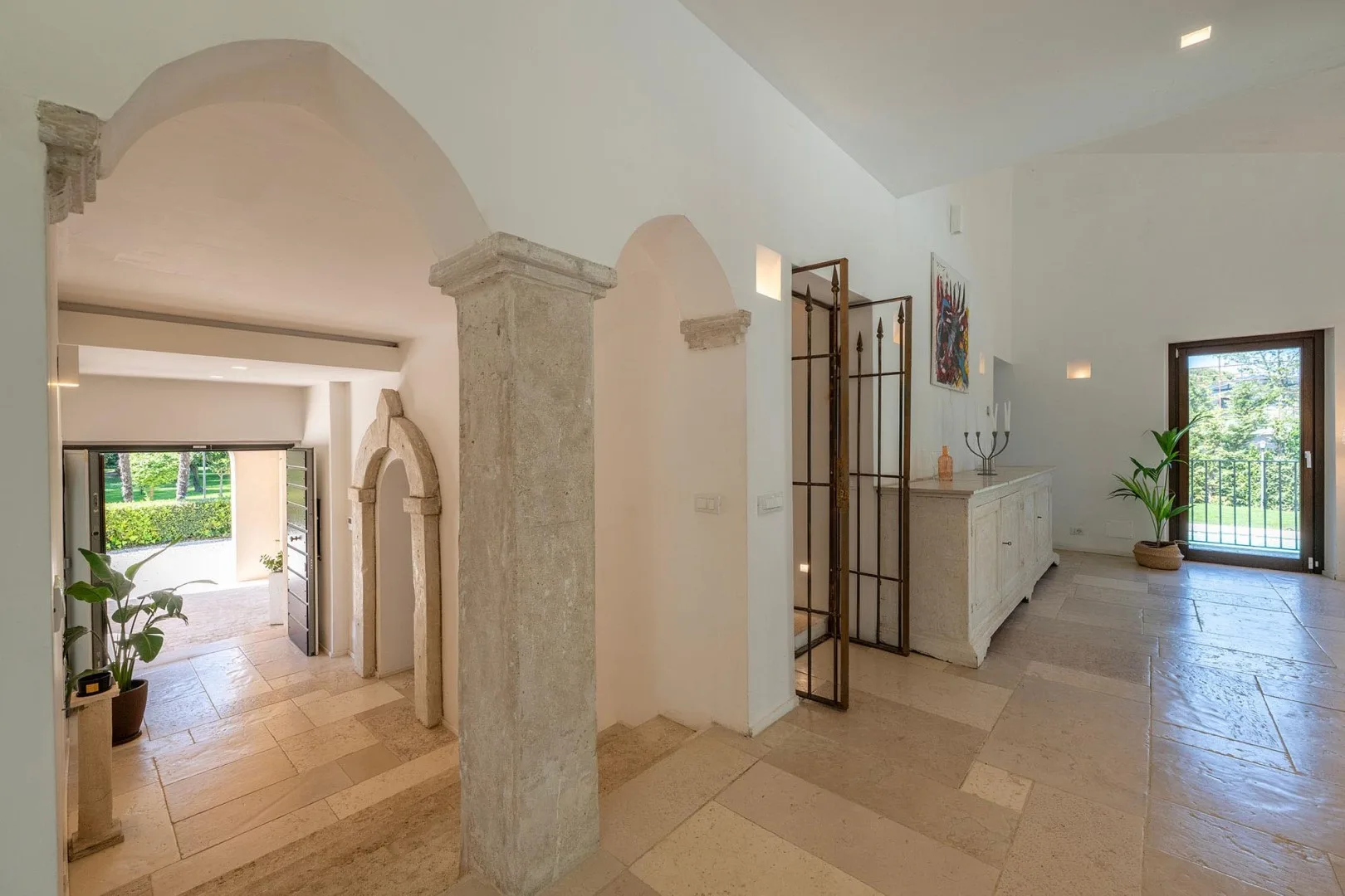 A bright interior hallway with stone arches, tiled floors, and a glass doorway.