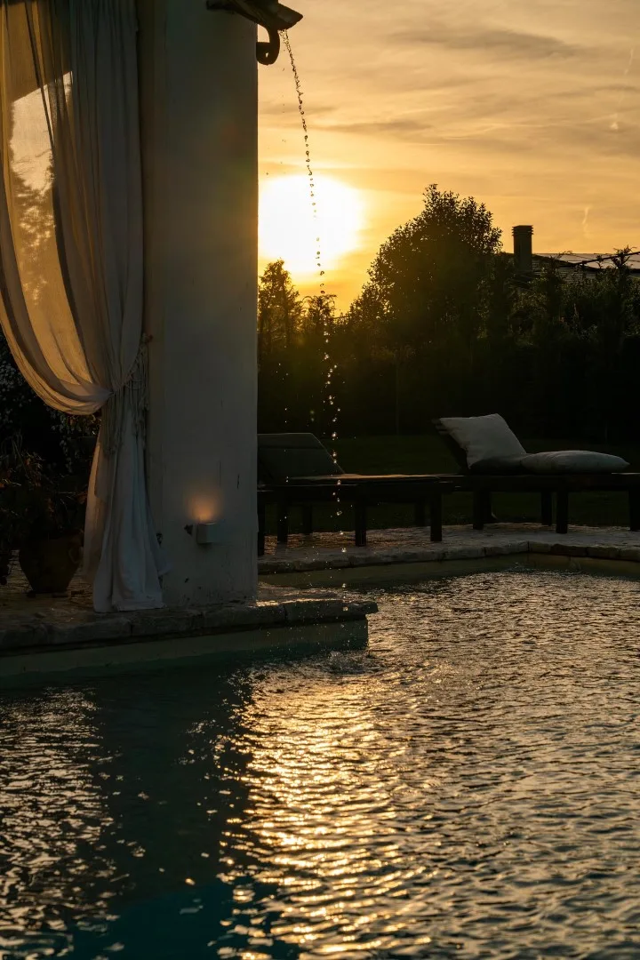 An outdoor pool reflects the setting sun beside seating and a flowing water feature.