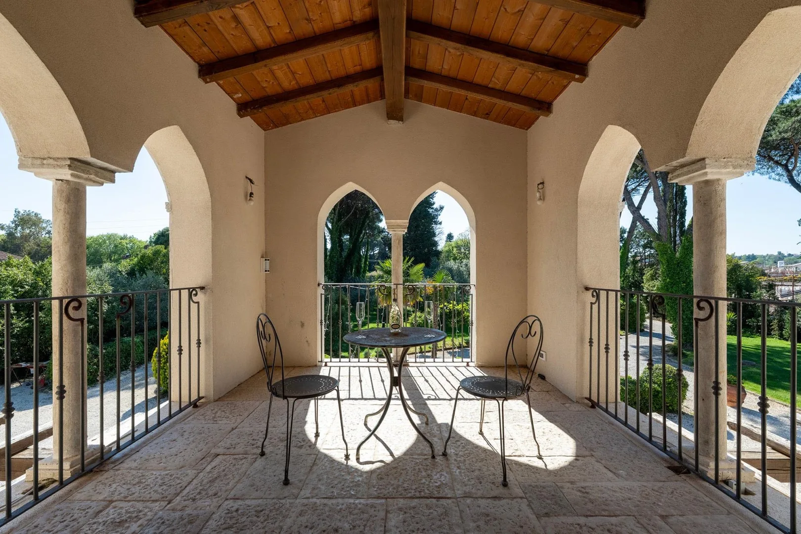 An arched outdoor terrace with a small table and metal seating overlooks greenery.