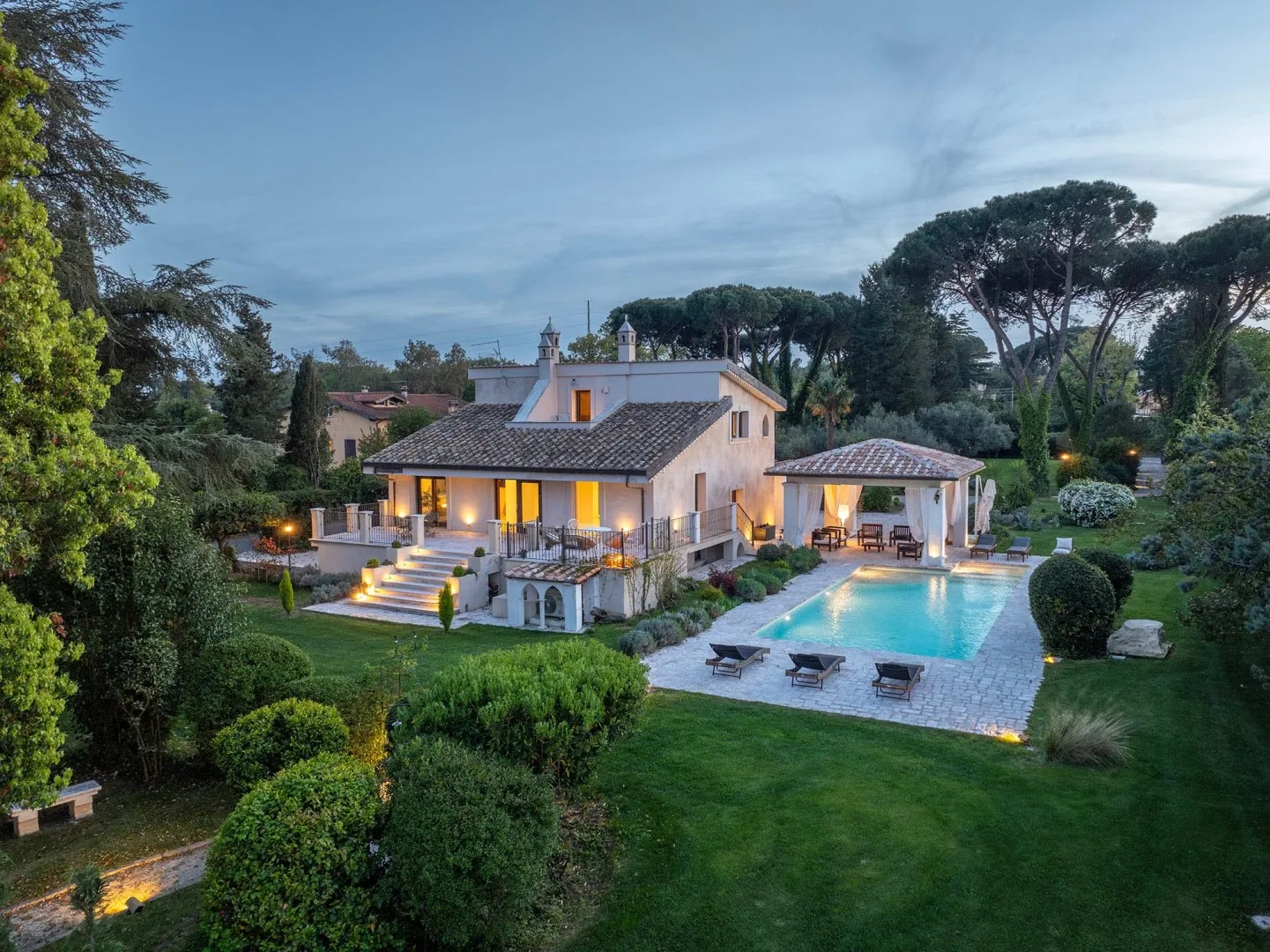 A house and outdoor swimming pool sit amid landscaped gardens at dusk.