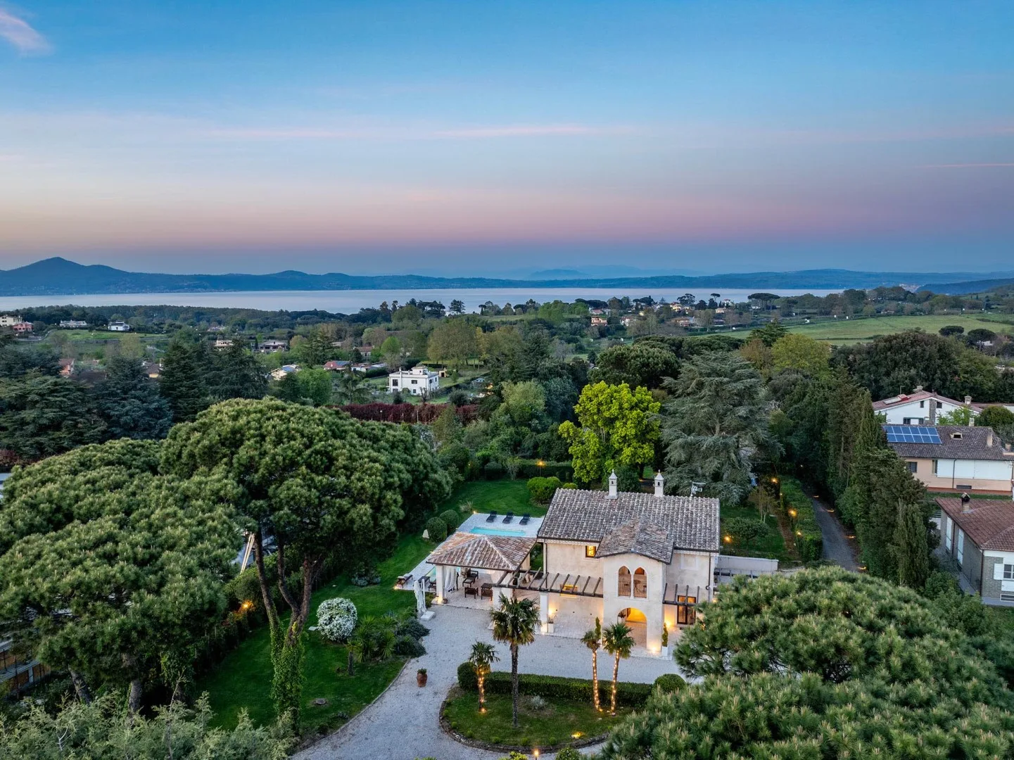 A house sits among green trees and gardens, with distant hills on the horizon.