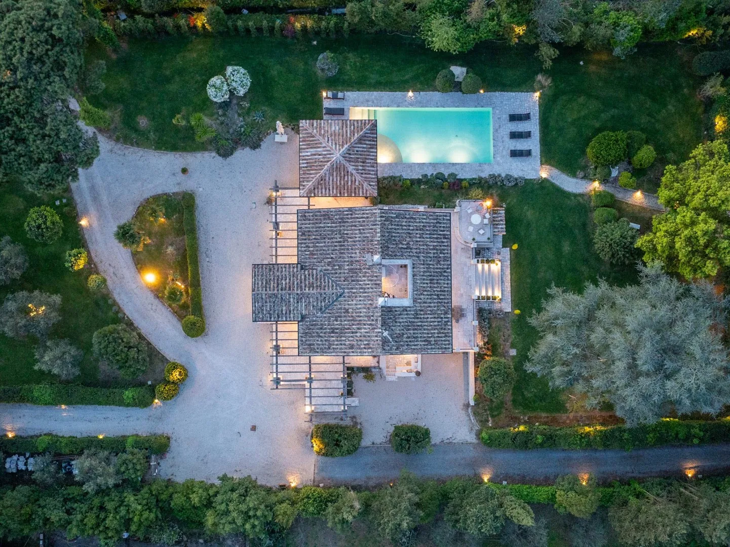 An overhead view of a house and swimming pool surrounded by trees and garden paths.