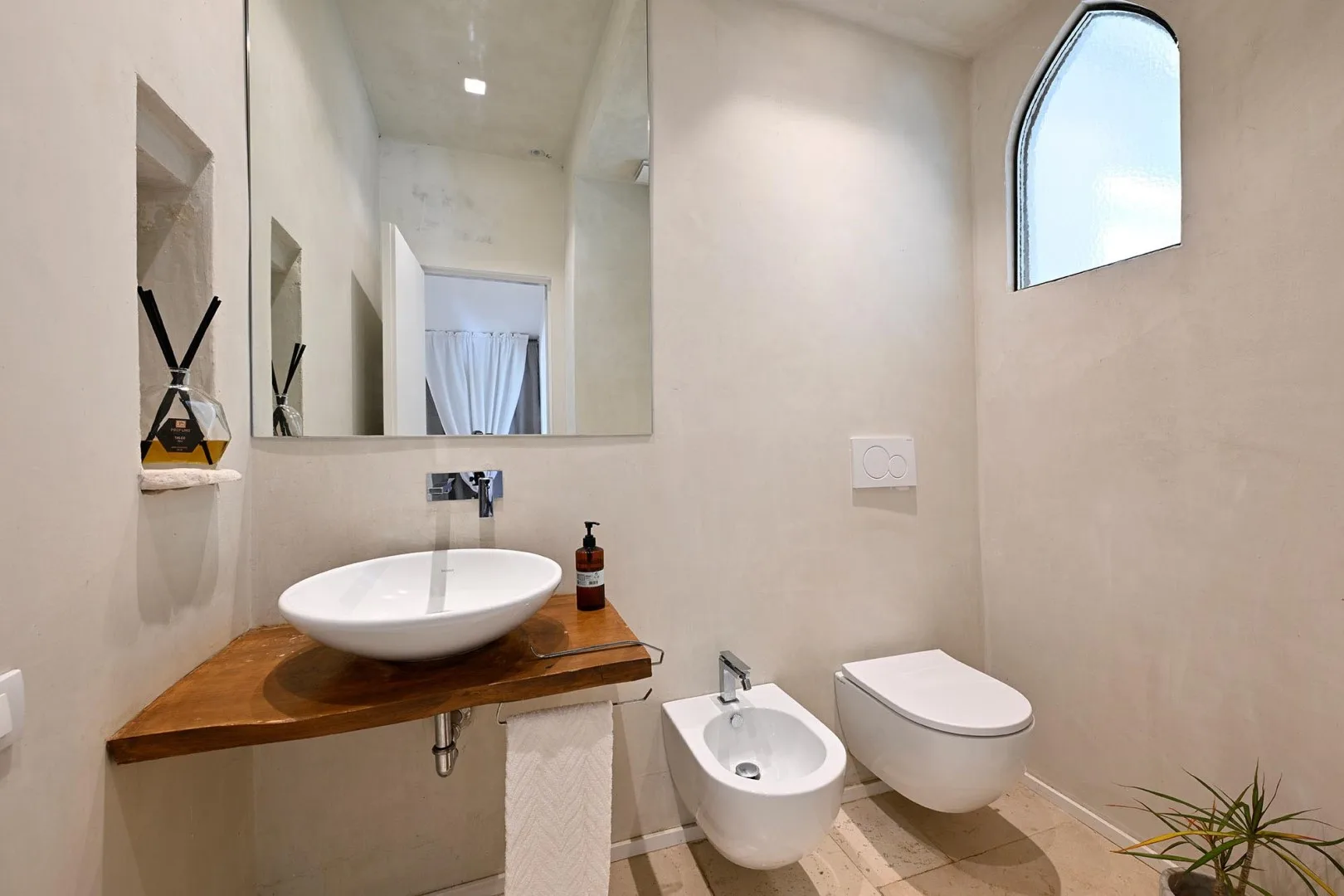 A bright bathroom with a vessel sink, bidet, and wall-mounted toilet.