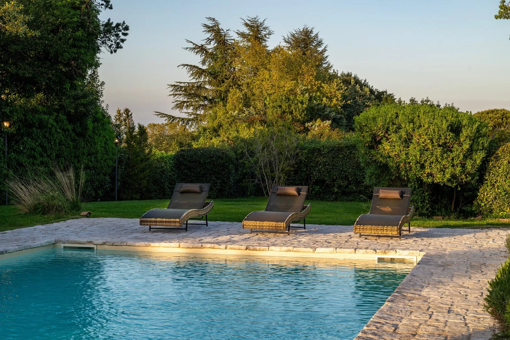 An outdoor swimming pool bordered by stone paving and reclining loungers.