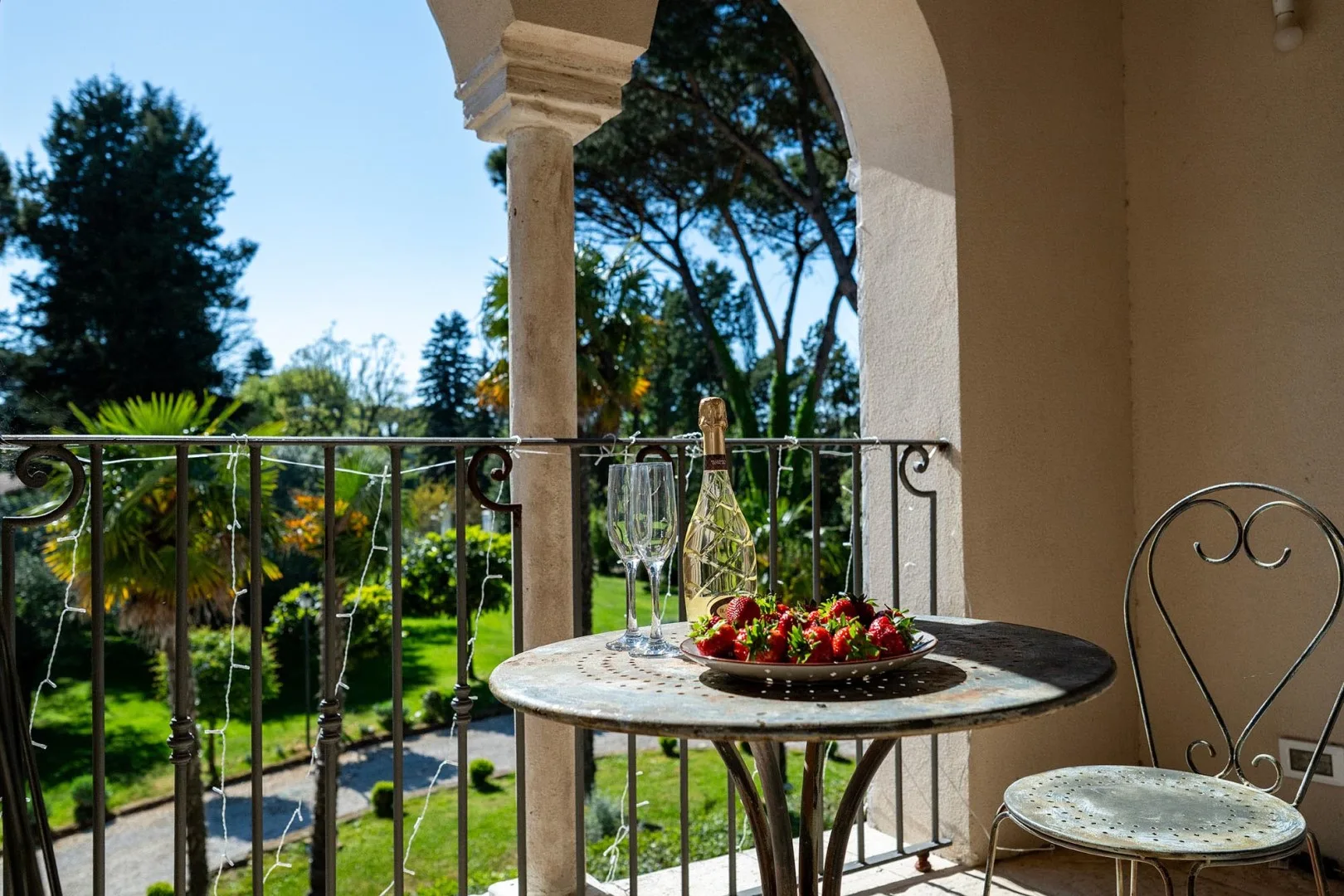A balcony table with a bowl of flowers overlooks a green garden.