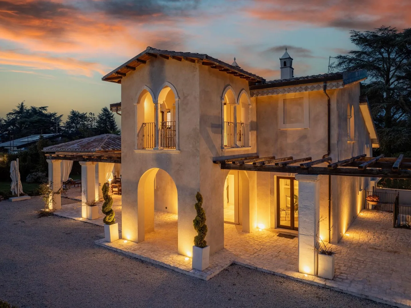 A warmly lit stucco building with arched openings stands beneath a colorful sunset sky.