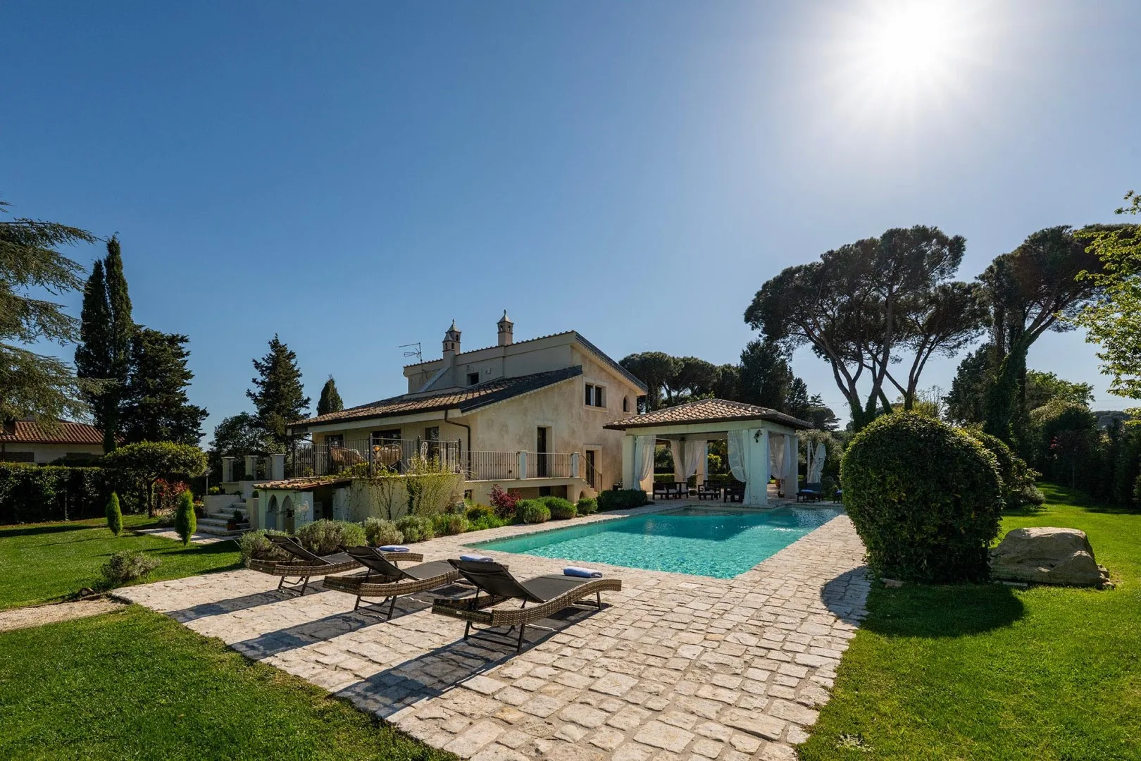 A sunny outdoor pool beside a stone patio and a house.